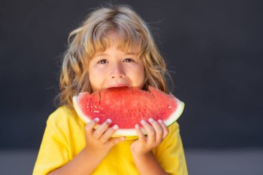 Çocuk yüzü ve karpuz, yaklaşın. Çocuk karpuz yiyor. Çocuk gri arka planda karpuz topluyor.