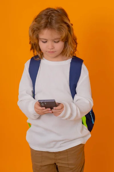 子供の孤立した肖像画 黄色のスタジオの背景に隔離された電話を使用してバックパックを持つ学校の子供 — ストック写真