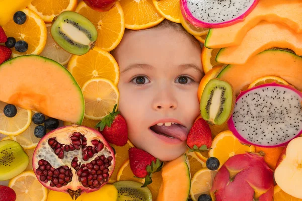 Kid lick strawberry. Funny child eats organic fruits. Healthy meal nutrition for children. Child eat tasty fruits. Fresh fruit and child face top view. Mix of raw fresh fruits