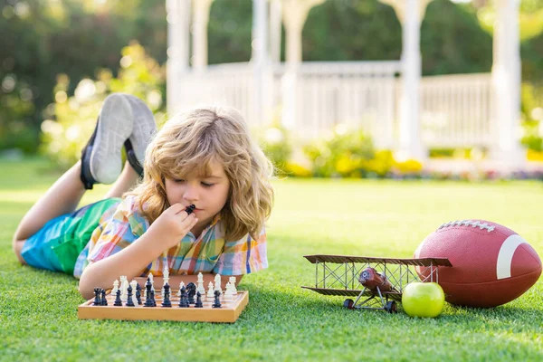 Summer games and outdoor activities for kids. Concentrated child boy developing chess strategy, playing board game in backyard, laying on grass