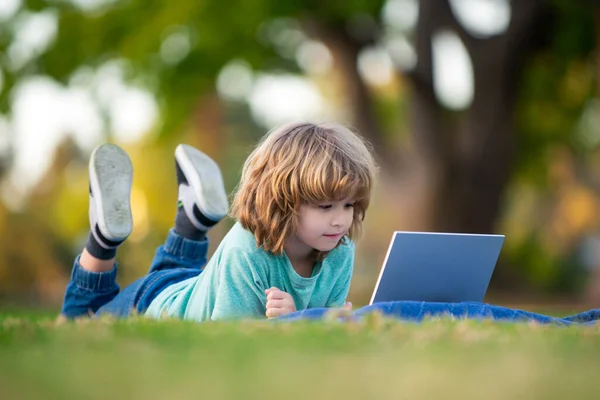 Pupil learning outdoor by studying online and working on laptop in park. Portrait of thinking child using laptop outside