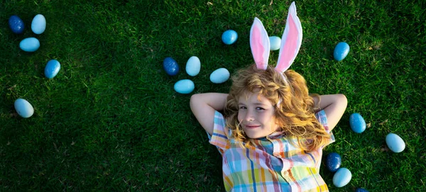 Portrait of bunny boy on Easter day. Top view of child boy hunting eggs in garden, spring family holidays. Horizontal photo banner for website header design