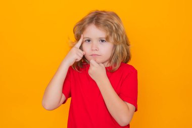 Çocuk sarı izole edilmiş arka plan hakkında bir şeyler biliyor. Sarı arka planda parmağını gösteren bir çocuk. Şok olmuş çocuk işaret ediyor, düşünüyor.