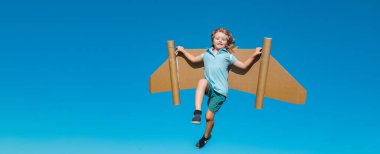 Mavi gökyüzüne karşı kağıt kanatlı mutlu çocuk. Oyuncak sırt roketli çocuk yeşil baharda dışarıda eğleniyor. Özgürlük tasasız ve çocukların hayal gücü kavramı