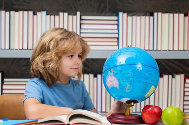 İlkokulun kütüphanesinde kürene bakan sevimli bir öğrenci. Okul çocuğu. İlkokuldan bir çocuk. Öğrenci, git çalış. Zeki okul çocuğu öğreniyor. Çocuklar öğrenim, bilgi ve eğitim