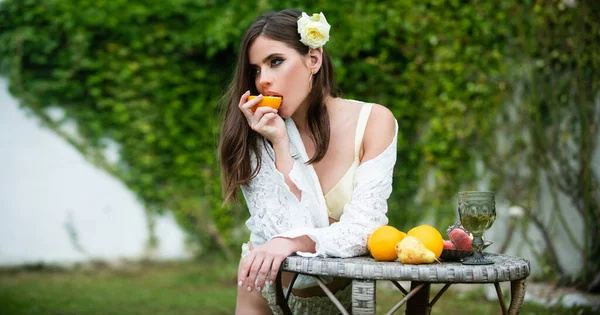 Sensual spring woman, banner for website header. Young sexy woman relaxing and eating orange fruit outdoor
