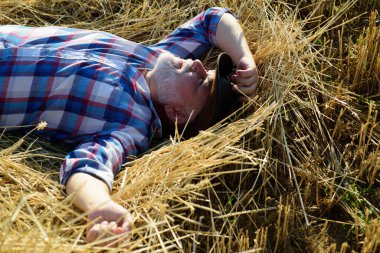 Senior farmer in the hay. Senior taking a break and relaxing on a hay on an summer day. Grandfather laying on haystack in countryside. Mature man resting at cereal field