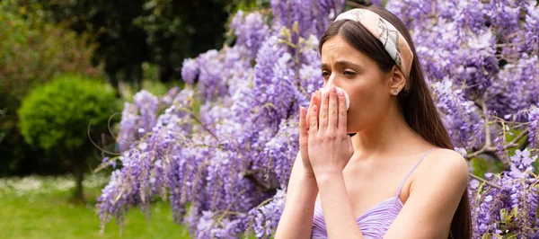 Spring allergy, flu. Banner. Girl with nose allergy sneezing. Polen illnes symptom concept. Woman allergic to blossom during spring blooming tree outdoor