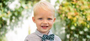 Close up portrait of cute child outdoors. Spring banner for website header. Happy child with bowtie, adorable lovely kid. Joyful portrait of small child on green nature background outside