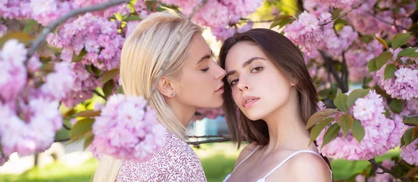 Sensual woman spring outdoor portrait banner. Young girls and spring flowers. Two beautiful young women in sakura flowers. Lesbian couple kissing. Sensual touch and kiss. Girlfriends couple