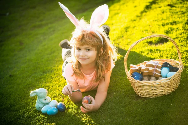 Child with easter eggs and bunny ears laying on grass. Funny boy, easter bunny kids. Happy Easter kids face