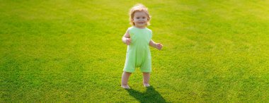 Baby on spring grass field, banner. Little baby learning to crawl steps on the grass. Concept childrens months. Happy child playing on green grass playground. First step