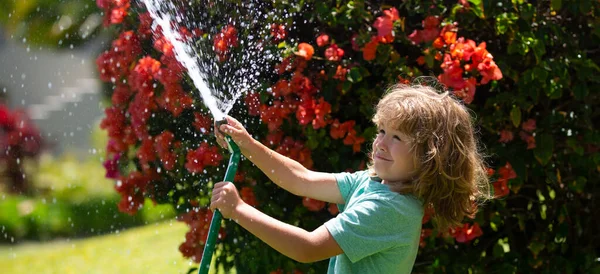 Spring child watering, banner. Cute little boy watering flowers in the garden at summer day. Child farmer with garden hose in planting plant. hose. Funny kid watering plants in the yard garden