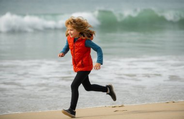 Child running through water close to shore along the sea beach. A boy runs along the sea coast. Rest of children on summer. Morning running with children. Outdoor sports and fitness for children