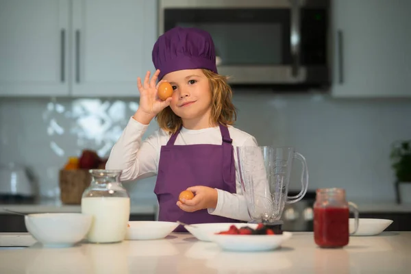 Child chef hold eggs. Funny child stand at kitchen table have fun baking cookies, doing bakery preparing dough making at home kithen