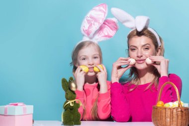 Mom with child girl are preparing for Easter. Mother and daughter wearing bunny ears are kissing. Easter banner, mockup copy space, poster flyer header for website template