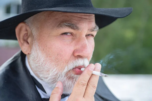 Close up portrait of funny stylish hipster grandfather in leather coat smoking outdoor