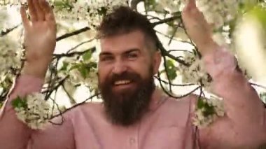 Çiçek açan çiçekli bahar sakallı adam, açık hava portresi. Çiçekli ağaçların yanında zarif bıyıklı vahşi sakallı esmer adam.