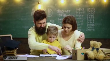 Young family studying. Family with little child boy reading book In playroom class. Happy cute clever boy. Child ready to answer with chalkboard on background. Ready for school