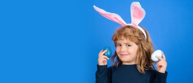 Easter banner, mockup copy space, poster flyer header for website template. Portrait of child with colorful Easter eggs isolated on blue background. Kids hunting easter eggs. Funny kids face