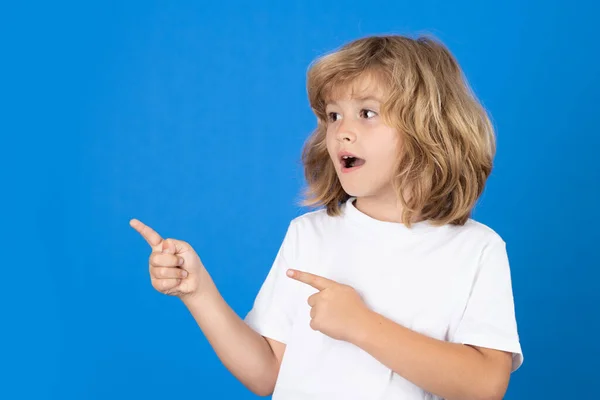 Excited child pointing finger on isolated studio background. Kid pointing to copyspace, showing promo offers, points away. Advertisement promo product concept