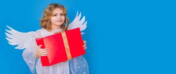 ギフトボックス付きの子供の男の子天使が存在します バレンタインデー 青い隔離されたスタジオの背景に天使の翼を持つブロンドのかわいい子供 コピースペース付きバナーヘッダー — ストック写真