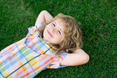 Kid summer. Child playing in garden. Happy little boy lying on the grass at the spring day