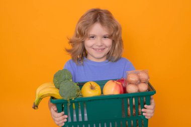 Portrait of child with shopping basket purchasing food in a grocery store on studio isolated background. Sale and discount