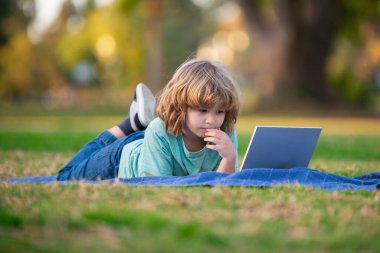 School boy in park outdoor doing school homework. Child using laptop. Self education learning studying. Early development for children