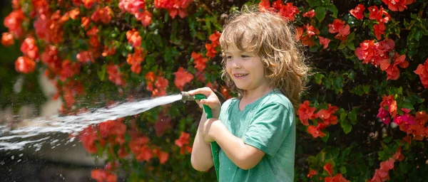 Spring child watering, banner. Funny little boy playing with garden hose in backyard. Child having fun with spray of water. Summer outdoors activity for kids