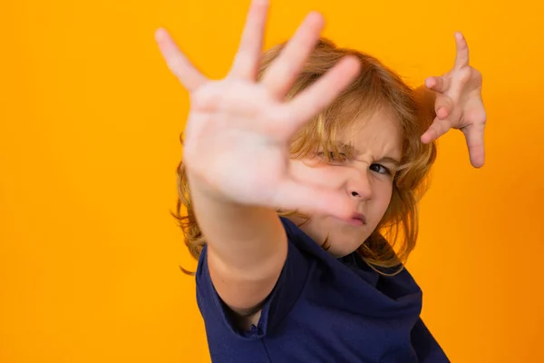 Child making stop gesture on yellow isolated studio background. Kid showing warning symbol, hand sign no. Kids protection, bullying, abuse concept