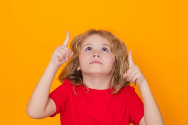 Portrait of kid pointing up finger on yellow background. Child pointing to copyspace, showing promo offers, points up