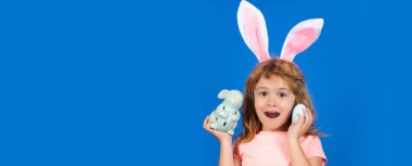 Excited child boy hunting easter eggs. Portrait of amazed, kid in rabbit costume with bunny ears having easter, isolated on blue background. Horizontal photo banner for website header design