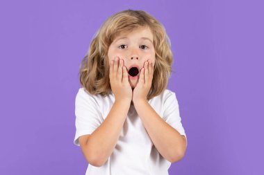 Shocked kid keeping hands near cheek with open mouth on studio isolated background. Surprised face, excited emotions of child. Shock, omg and wow expression