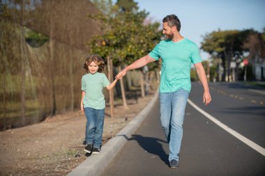 Father and son walking on road holding hands spending time outdoor together. Urban city walk family