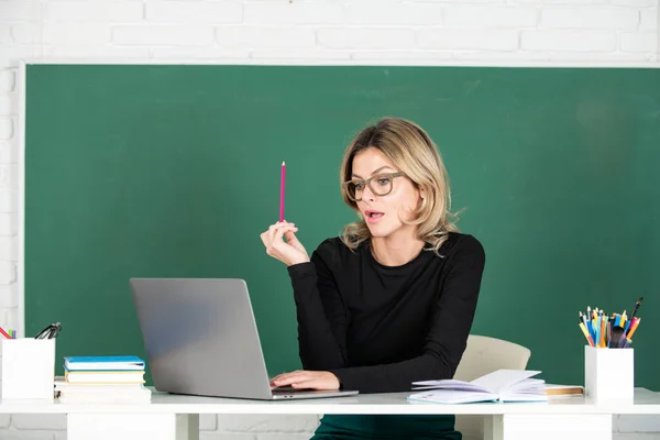 Modern attractive teacher. Portrait of smart young woman in glasses with book on the blackboard in class at high school or collage. Female professor at school, ready to start lesson