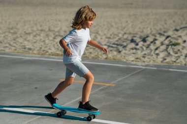 Child riding skateboard in summer park. Little boy learning to ride skate board. Active outdoor sport. Children skateboarding. Kid ride on skateboard. Lets ride. Child ride on penny board on street