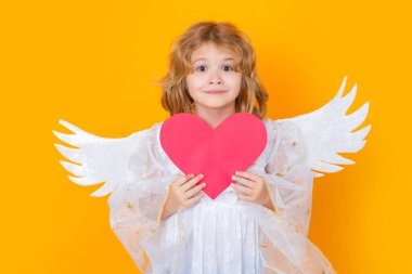 Angel child with heart. Valentines day. Blonde cute child with angel wings on a yellow studio background. Happy angel child