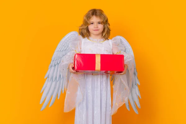 Angel with gift box present. Valentines day. Blonde cute child with angel wings on a yellow studio background. Happy angel child