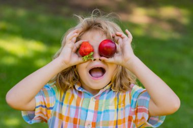 Summer funny kid face. Strawberry fot kids. Happy kid eating ripe, sweet, juicy, fresh strawberry. Child holding strawberries. Concept of healthy summer berries strawberries