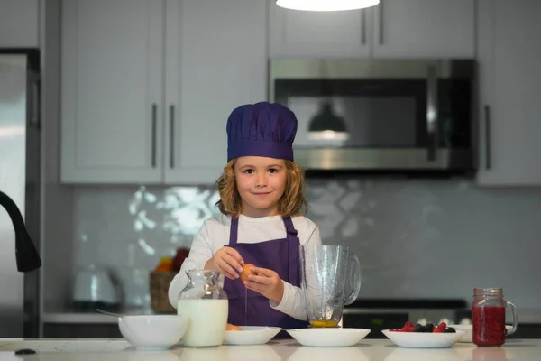 Cooking in kitchen. Child in chef hat and apron preparing in the kitchen
