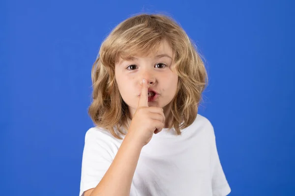 Kid with show no talk gesture. Boy with shows shh sign. Be quiet. Hush dont tell. Child put finger to lips mouth, ask stop share rumor, isolated on blue studio isolated background