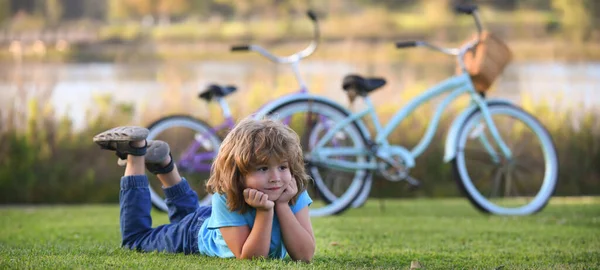 Little boy lying on the grass at the summer park. Portrait of a smiling child lying on green grass outdoor. Spring and kid. Wide photo banner for website header