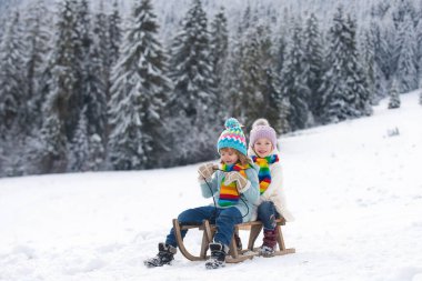 Winter scene with snowy forest. Little boy and girl sledding in winter. Kids sibling riding on snow slides in winter. Son and daughter enjoy a sleigh ride