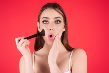 Studio portrait of a woman applying cosmetic tonal foundation on face using makeup brush. Beautiful girl doing contouring apply blush on cheeks isolated on studio background