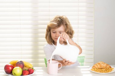 Cute child pouring whole cows milk. Portrait of child eat fresh healthy food in kitchen at home. Kid boy eating breakfast before school
