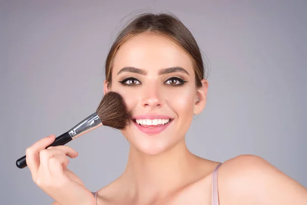 Beautiful woman applying make-up powder on the cheek. Cosmetic powder brush. Perfect skin and natural makeup