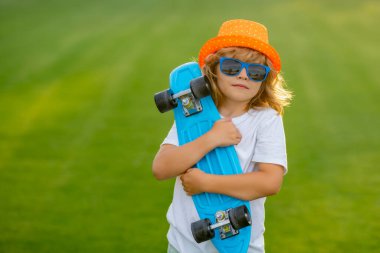 Summer kids. Childhood and fashion. Cute child with skateboard on summer park background. Funny kid boy, stylish skater holding skateboard outdoor
