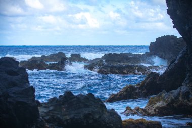 Deniz taşlarla ve kumsalın kumuyla çarpışıyor. Deniz dalgaları taşa çarpıyor.