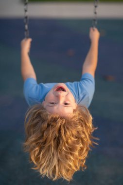 Funny child boy on swing. Kid swinging on playground. Cute excited amazed child on swing. Cute child swinging on a swing. Crazy playful child swinging very high